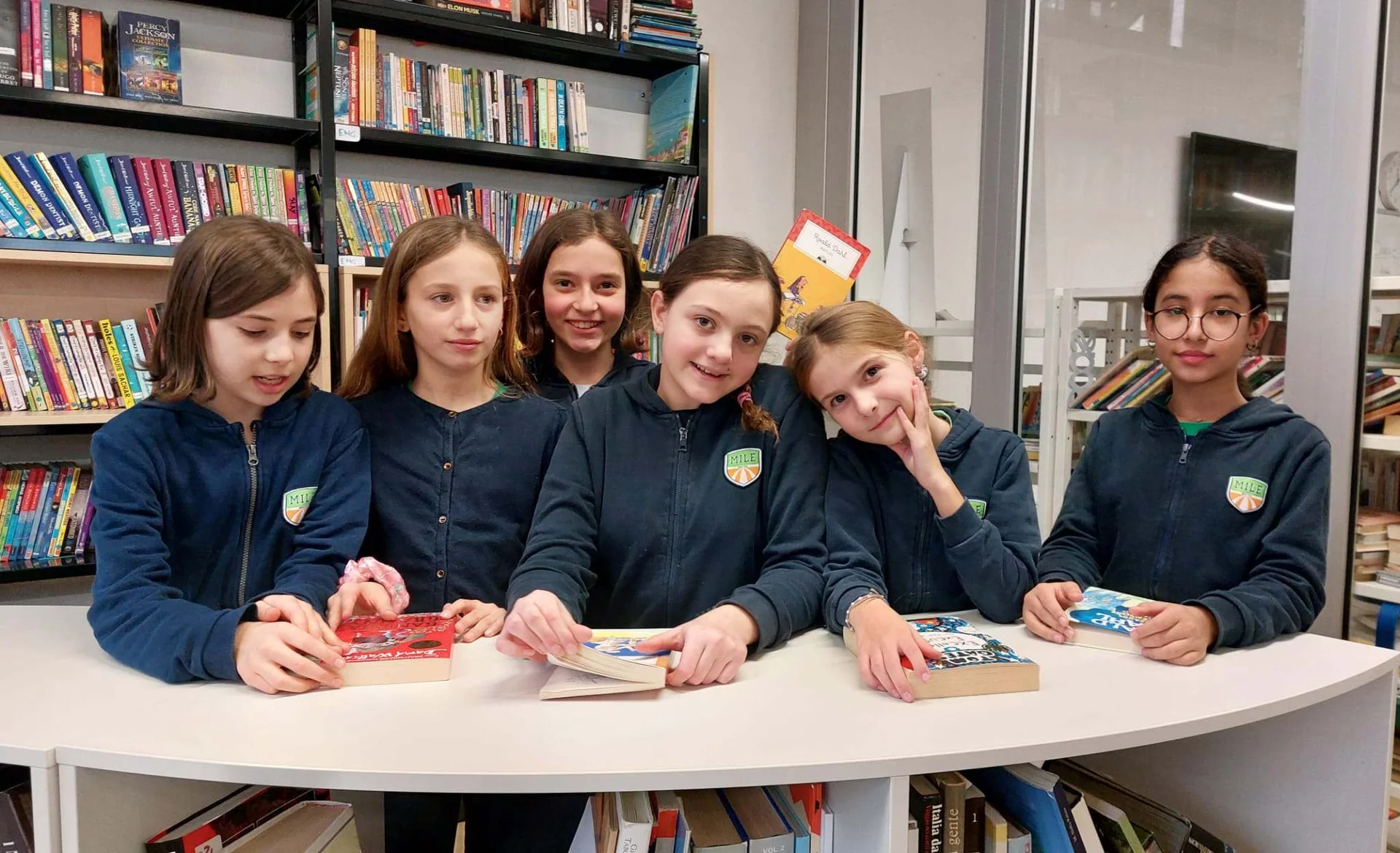 Students in navy MILE uniforms browsing and reading books together in a library