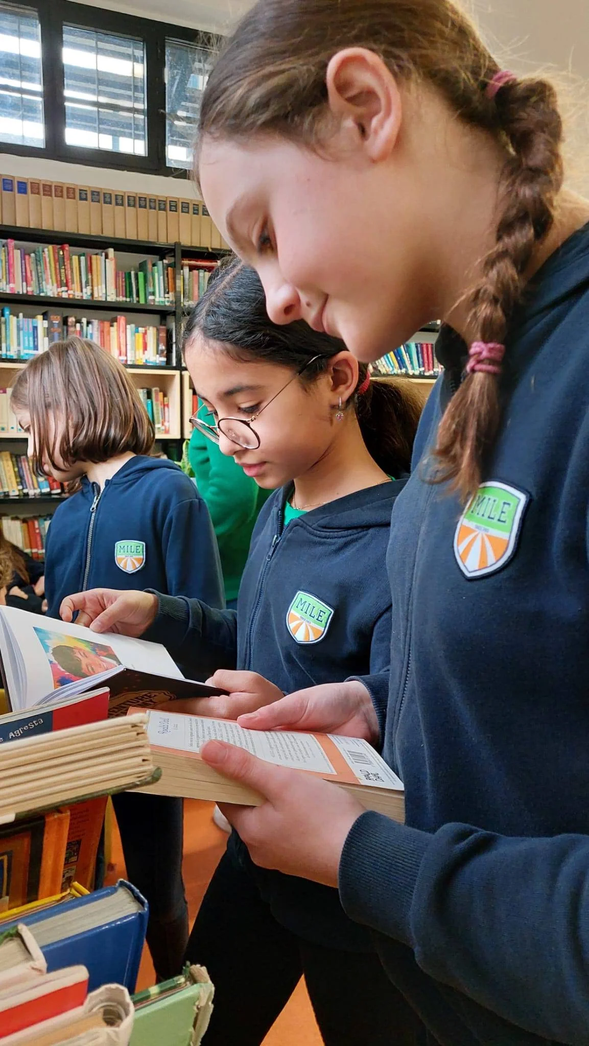 Students in navy MILE uniforms browsing and reading books together in a library
